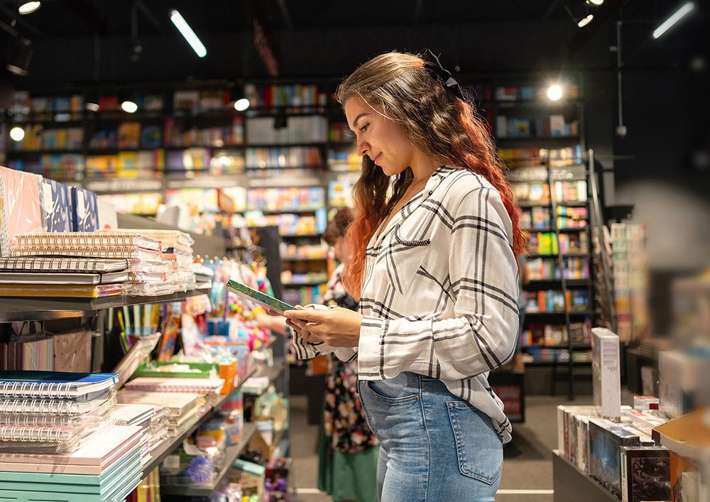 Frau steht in einer Buchhandlung vor einem Regal und blättert in einem Buch.