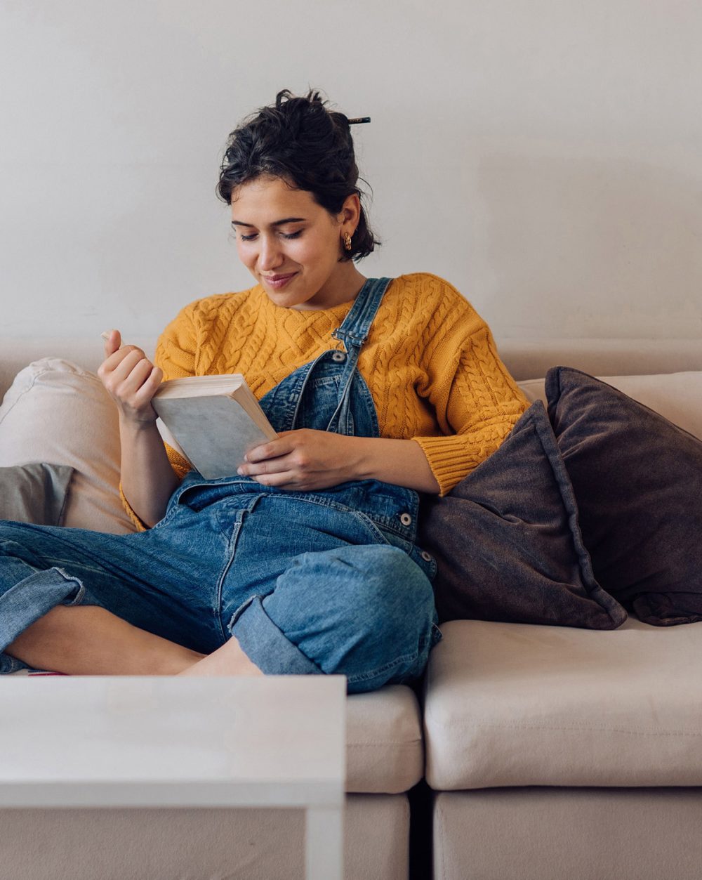 Frau liest entspannt auf dem Sofa ein Buch zu Hause