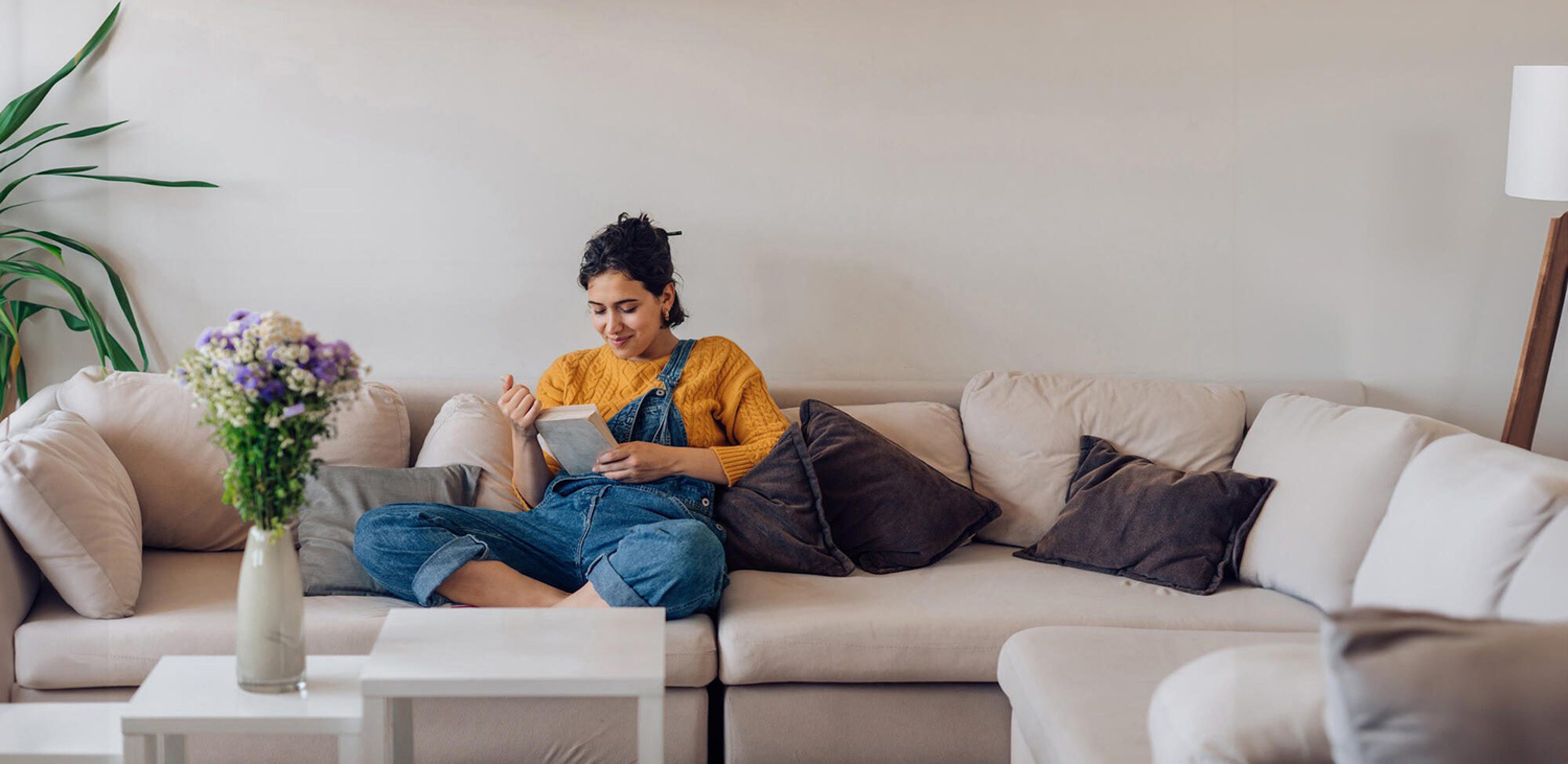 Frau liest entspannt auf dem Sofa ein Buch zu Hause